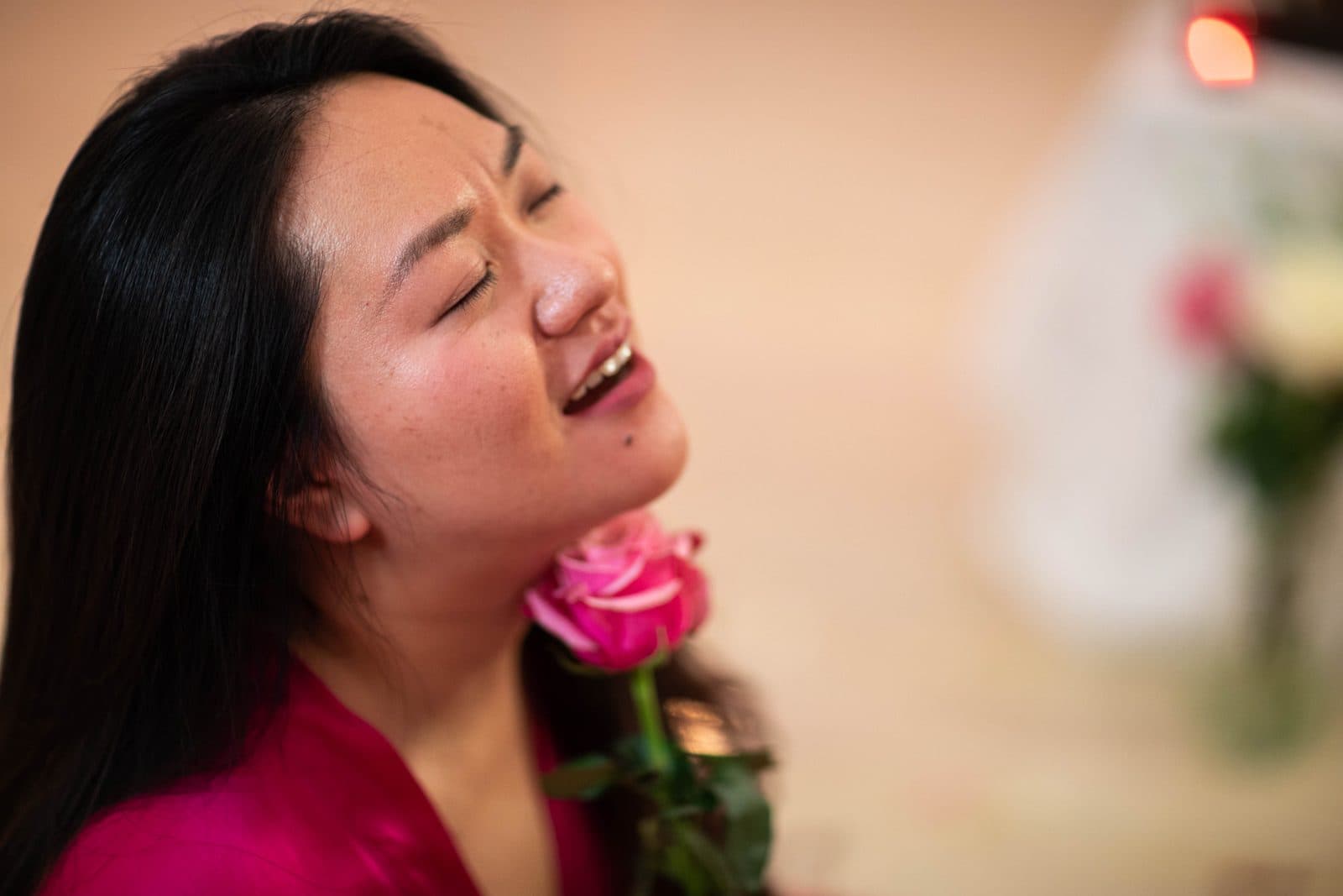 A woman with her eyes closed, a pink rose held to her cheek