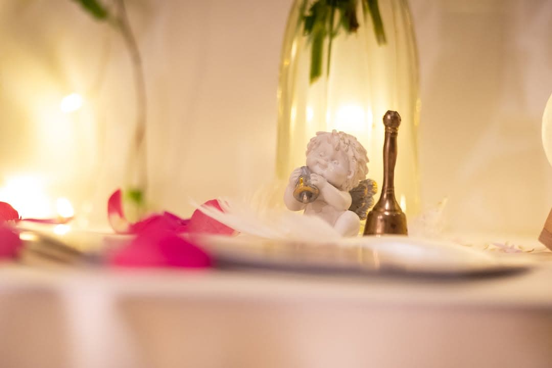 An angel figurine and a small bell among rose petals and candlelight
