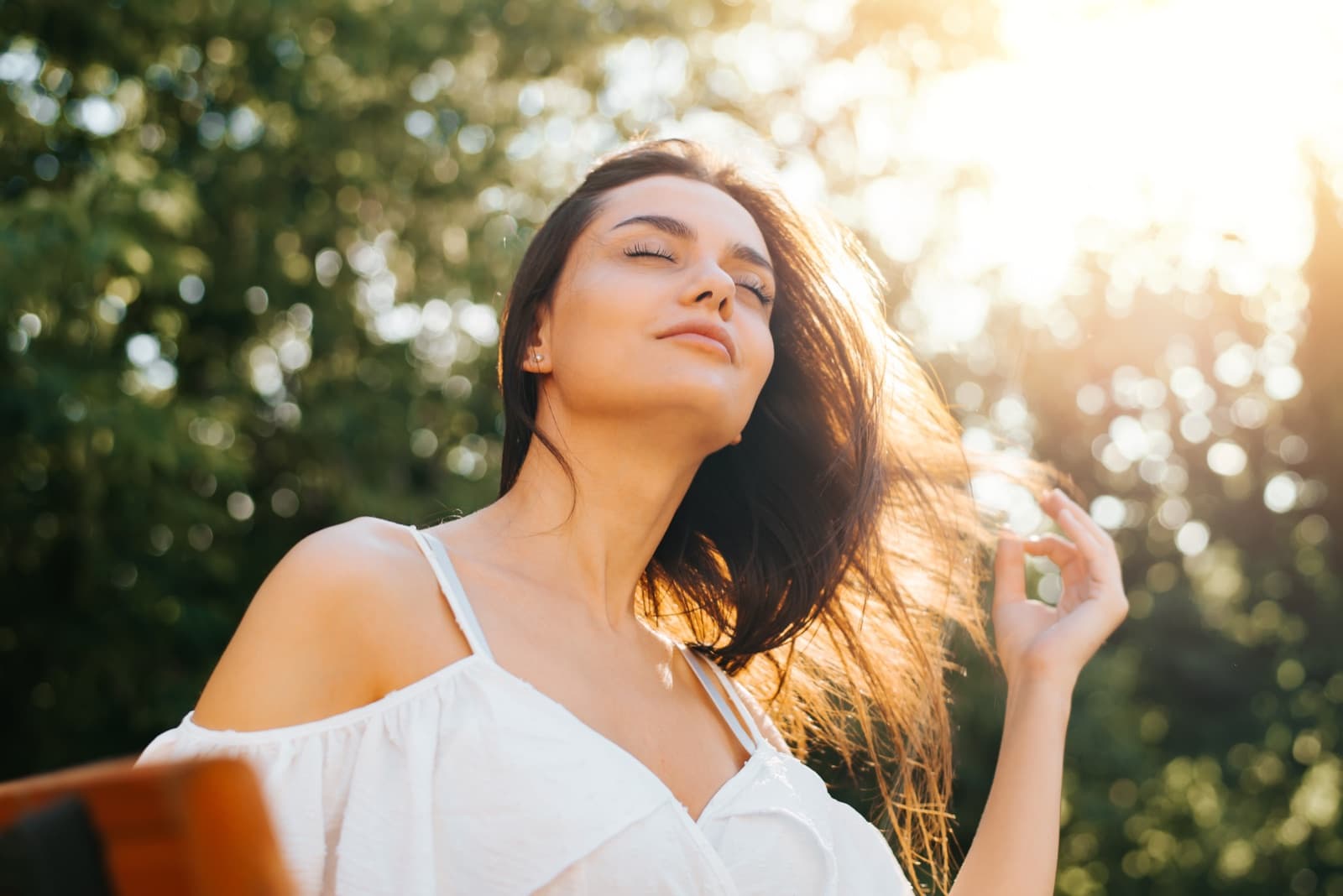 A woman with her eyes closed, face lifted to the evening sun among the trees