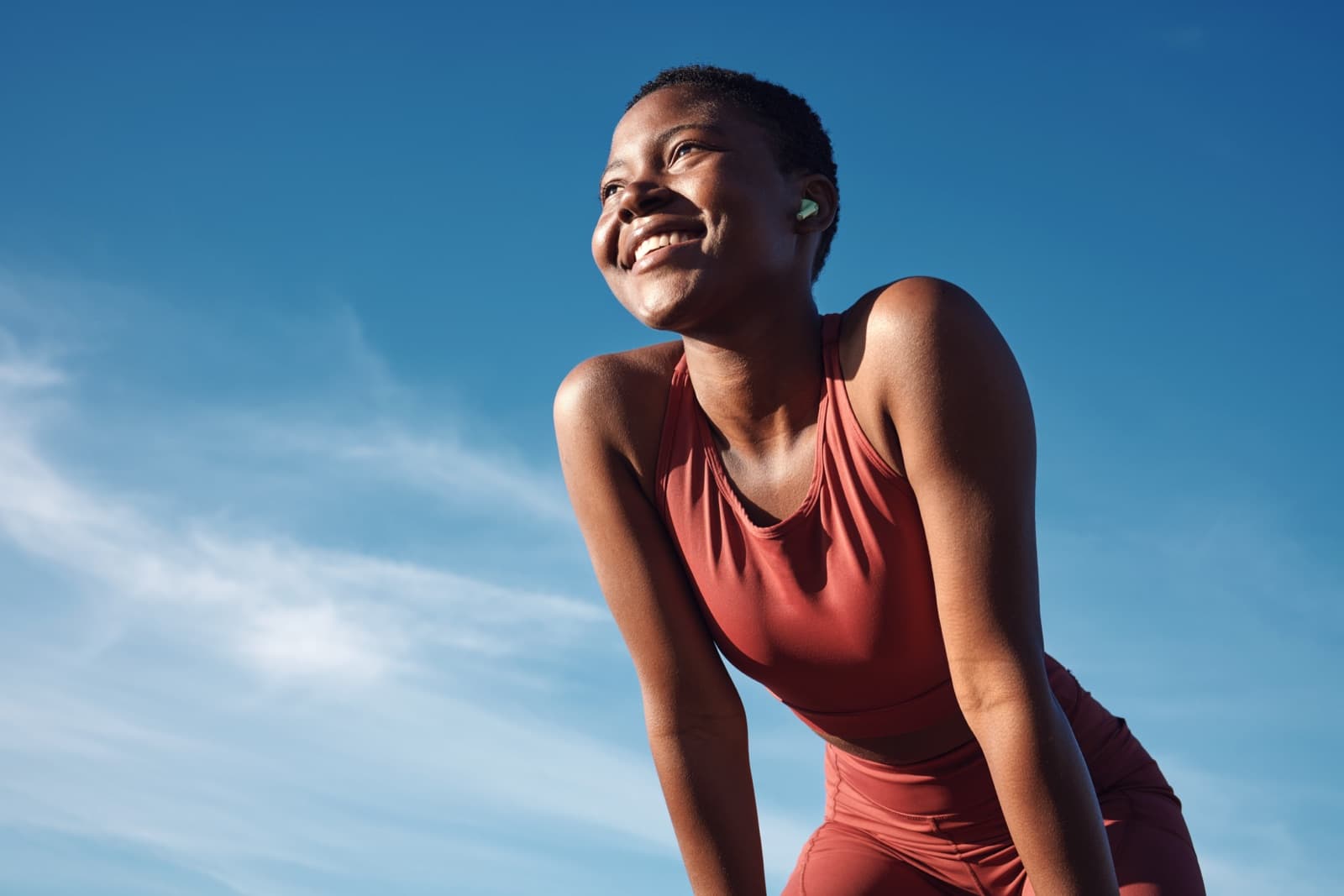 A woman in red sportswear laughing against a clear blue sky